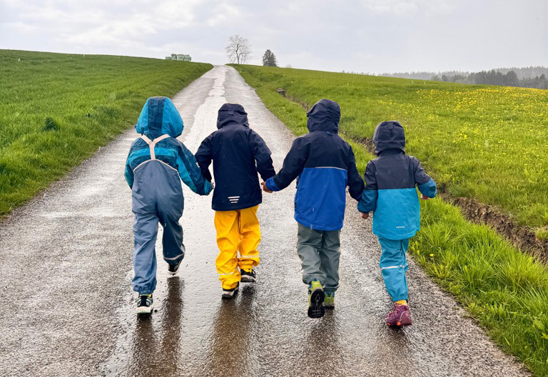 Kleine Kinder in Regensachen laufen fröhlich einen Feldweg entlang