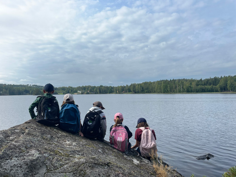 Kinder sitzen auf einem Felsen und schauen auf einen großen See
