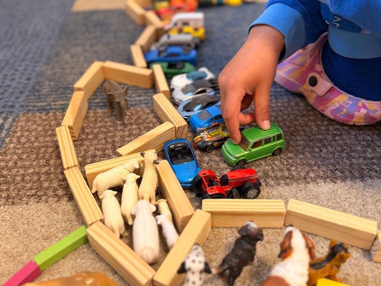 Kind spielt mit Holzklötzen, Autos und Tieren